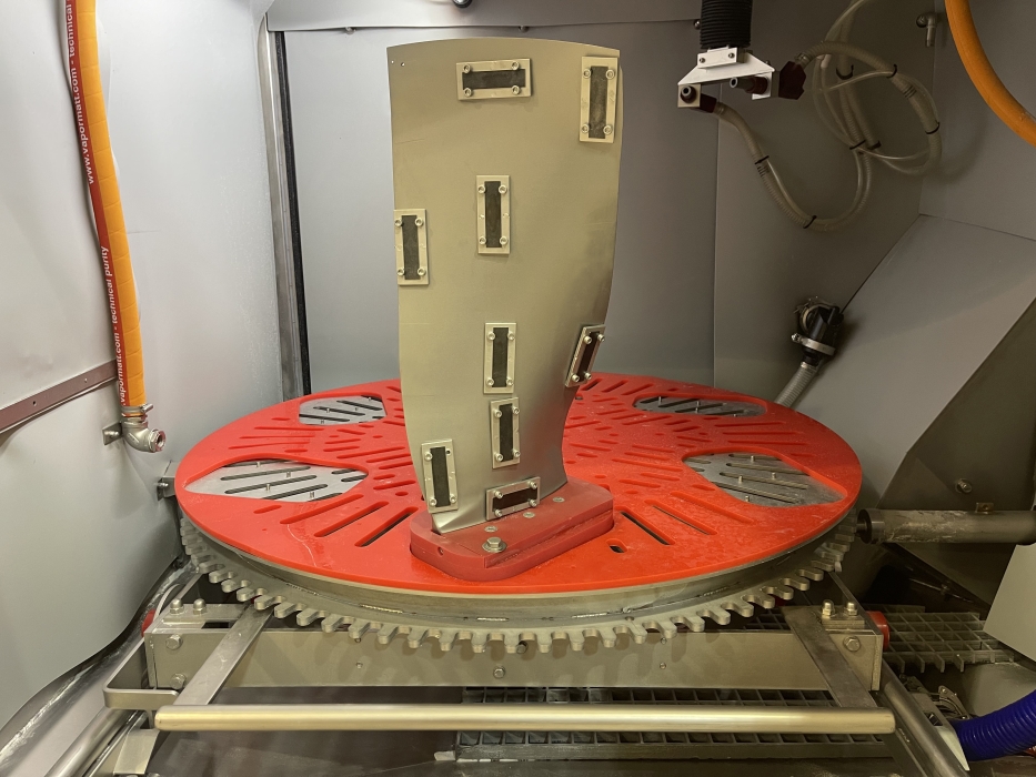A jet engine fan blade mounted in a Cougar+ wet blasting machine with Almen strips fitted for peening measurement