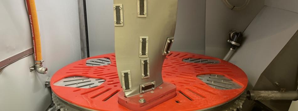 A jet engine fan blade mounted in a Cougar+ wet blasting machine with Almen strips fitted for peening measurement